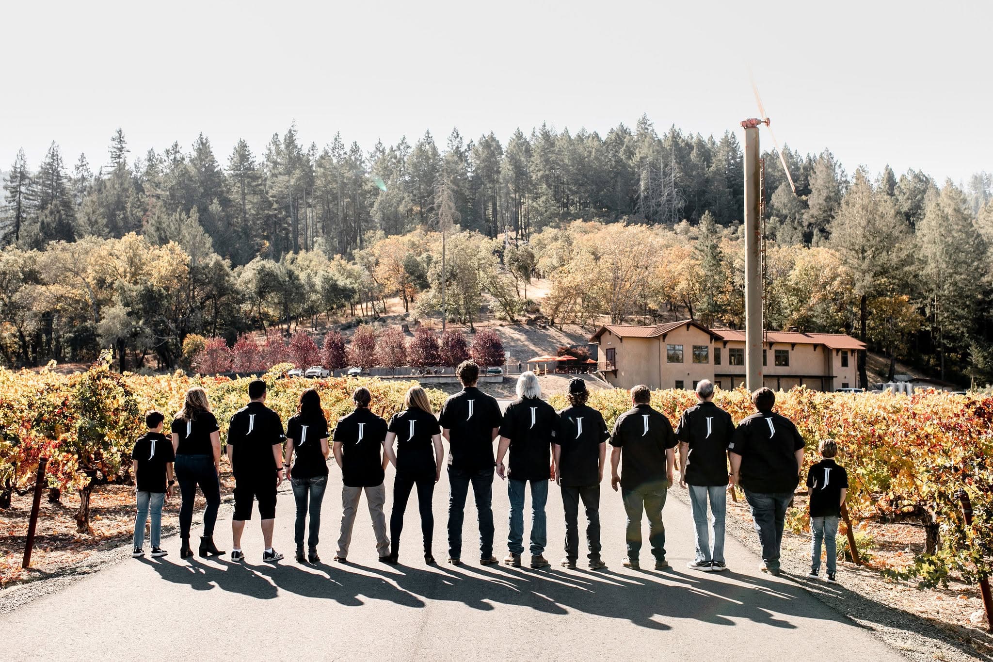 The Joseph Cellars family and team in matching J shirts, looking across the autumn vineyard to the winery